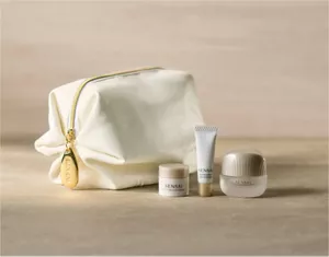 Ein luxuriöses weißes Kosmetiktäschchen mit goldenem Reißverschluss neben drei Hautpflegeproben auf einer grauen Marmoroberfläche bei dezenter Beleuchtung